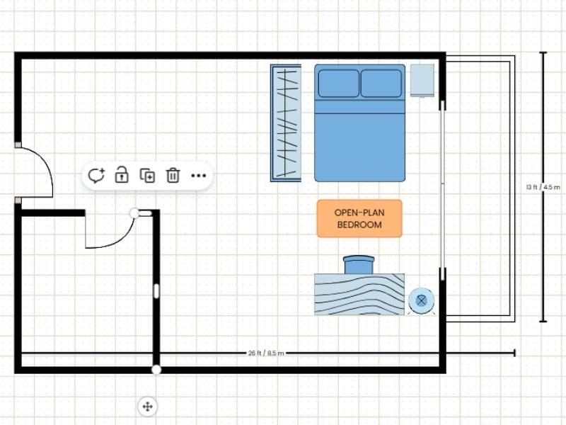 2D floor plan made with a template in Canva. It shows how to edit in the template. Two walls are dragged down to extend the smaller room. The floor plan shows a two-room floor plan with a balcony and blue furniture such as a double bed, a closet, a nightstand, a desk with a chair and a lamp. There is also an orange label saying "open-plan bedroom". There are measurements showing the size of the floor plan outside the walls of the floor plan.