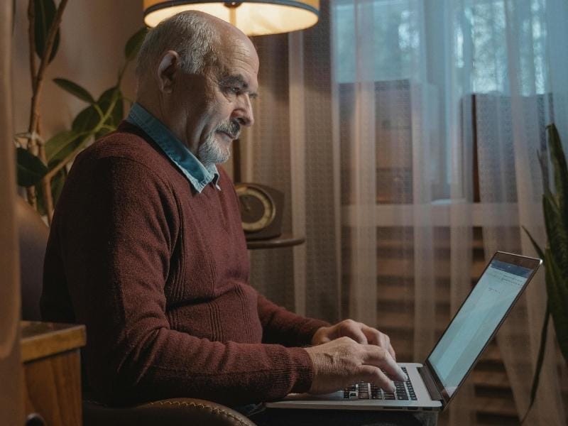 An elderly move management client sitting at his new home's 'command center' with a laptop.
